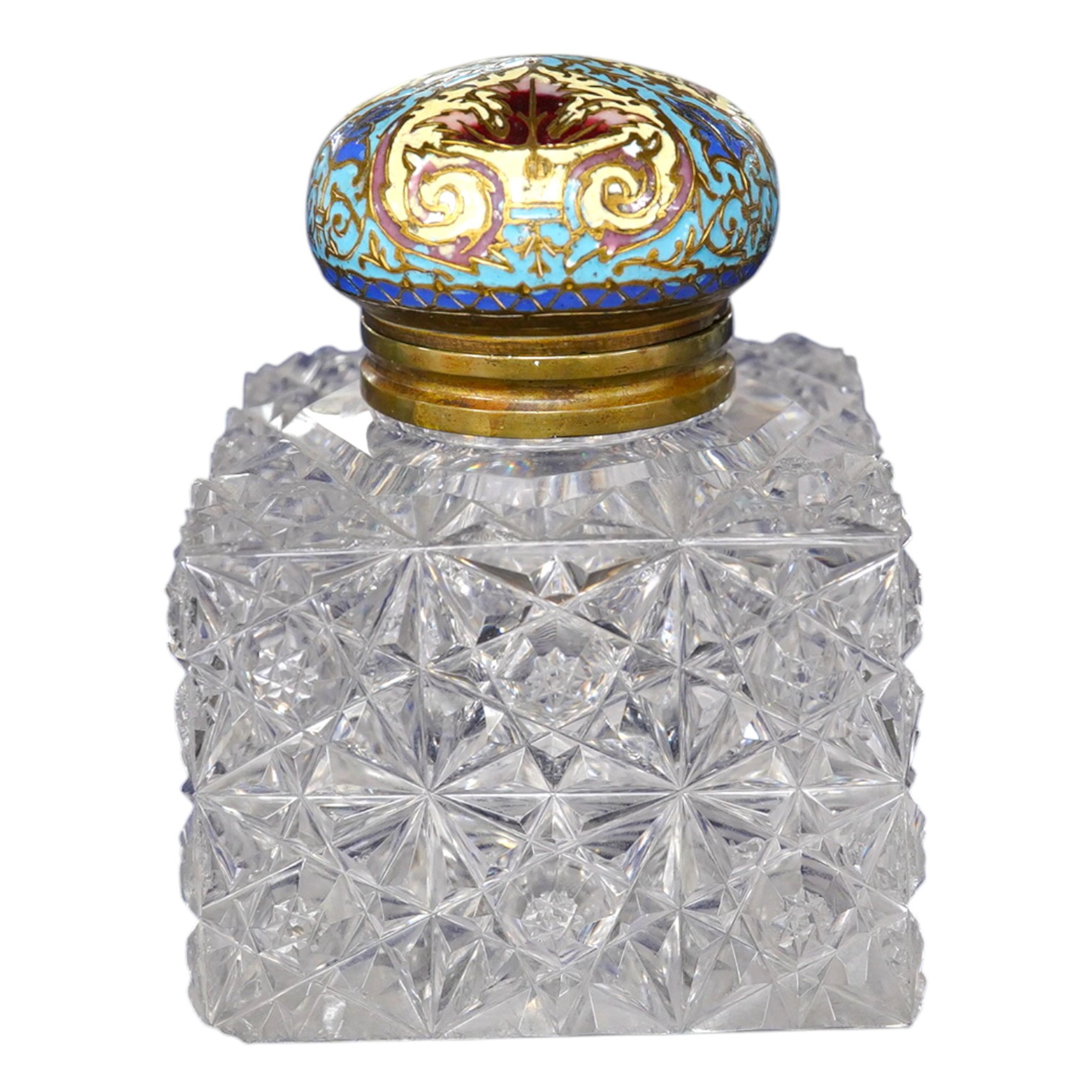 A large square glass inkwell, heavily cut with star cut base and octagonally cut top with enamelled brass hinged cover, 8cm wide. Condition - fair, some chipping